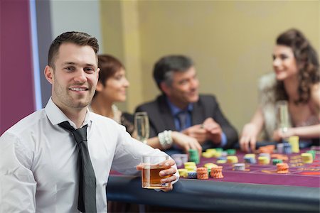 simsearch:400-06802091,k - Young man with whiskey looking up and smiling from roulette table Stock Photo - Budget Royalty-Free & Subscription, Code: 400-06801997