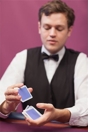 Dealer sitting at table in a casino while shuffling deck of cards Stock Photo - Budget Royalty-Free & Subscription, Code: 400-06802053