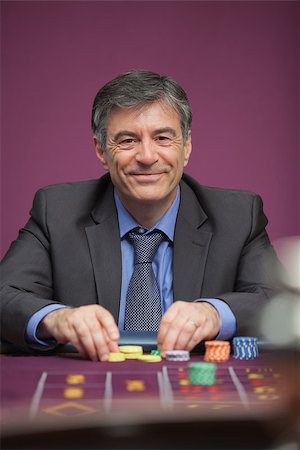 Smiling man sitting at table in a casino while playing roulette and grabbing chips Stock Photo - Budget Royalty-Free & Subscription, Code: 400-06802088