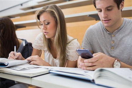 simsearch:400-06803206,k - Student using smartphone in lecture hall with other student studying Stock Photo - Budget Royalty-Free & Subscription, Code: 400-06803268