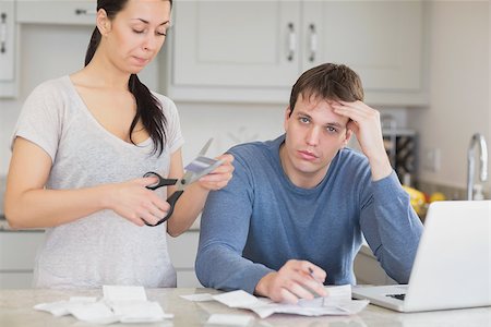simsearch:400-06803524,k - Disappointed woman cutting through a credit card with stressed husband in kitchen Stock Photo - Budget Royalty-Free & Subscription, Code: 400-06803535