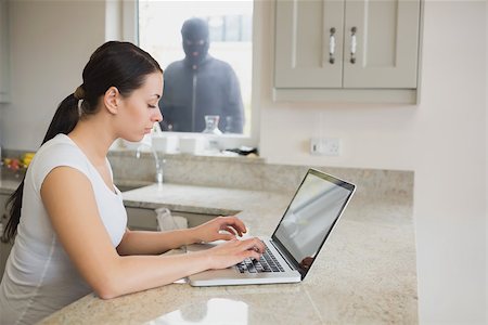 simsearch:400-06881880,k - Woman using a laptop in the kitchen with burglar standing at the window Stockbilder - Microstock & Abonnement, Bildnummer: 400-06803556