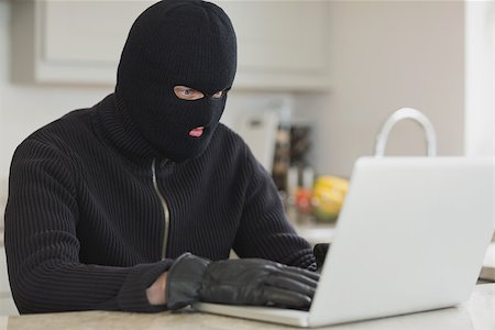 simsearch:694-03328255,k - Burglar sitting in the kitchen and hacking a laptop Photographie de stock - Aubaine LD & Abonnement, Code: 400-06803551