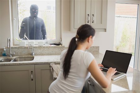 Woman on laptop in kitchen being observed by burglar through window Foto de stock - Super Valor sin royalties y Suscripción, Código: 400-06803562