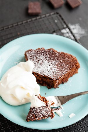 Closeup of slice of chocolate cake and whipped cream on plate resting on mesh metal tray with chocolate squares in background Photographie de stock - Aubaine LD & Abonnement, Code: 400-06859037