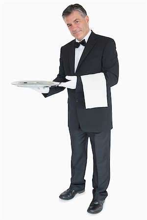 plateau d'argent - Smiling waiter standing against the white background holding silver tray with towel over his arm Photographie de stock - Aubaine LD & Abonnement, Code: 400-06865611