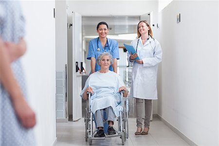 simsearch:400-07337135,k - Smiling nurse assisting senior woman sitting in a wheelchair in a hospital corridor Stock Photo - Budget Royalty-Free & Subscription, Code: 400-06867983