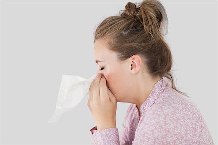 simsearch:400-06801081,k - Closeup of young woman blowing her nose agaist grey background Photographie de stock - Aubaine LD & Abonnement, Code: 400-06868915