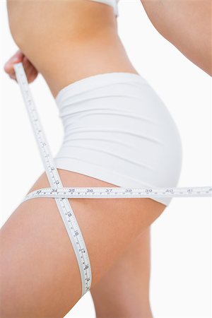 Midsection of woman measuring thigh with measuring tape over white background Stock Photo - Budget Royalty-Free & Subscription, Code: 400-06869724