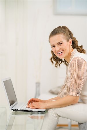 simsearch:400-06419734,k - Smiling young woman sitting on couch in living room and using laptop Stock Photo - Budget Royalty-Free & Subscription, Code: 400-06861285