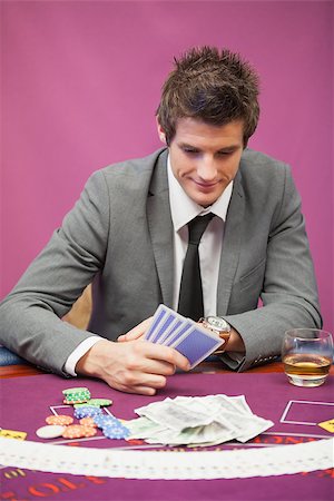 Smiling man sitting at table in a casino while playing poker and holding cards Stock Photo - Budget Royalty-Free & Subscription, Code: 400-06862368