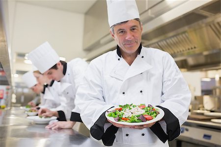 simsearch:400-06863053,k - Cheerful chef presenting his salad with others preparing salads in kitchen Stockbilder - Microstock & Abonnement, Bildnummer: 400-06863019