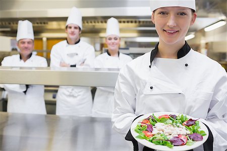 simsearch:400-06863053,k - Smiling chef holding out a salad in the kitchen with team standing behind her Stockbilder - Microstock & Abonnement, Bildnummer: 400-06863069
