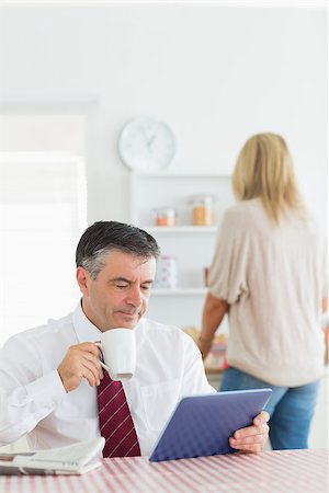 Man sitting at the kitchen holding a cup of coffee and using tablet pc before work Stock Photo - Budget Royalty-Free & Subscription, Code: 400-06863474