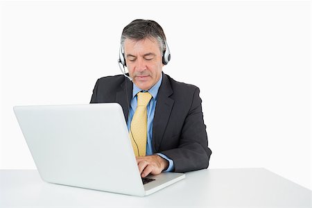 Serious man sitting at his desk with headphones writing on the laptop and talking on a white background Stock Photo - Budget Royalty-Free & Subscription, Code: 400-06863761
