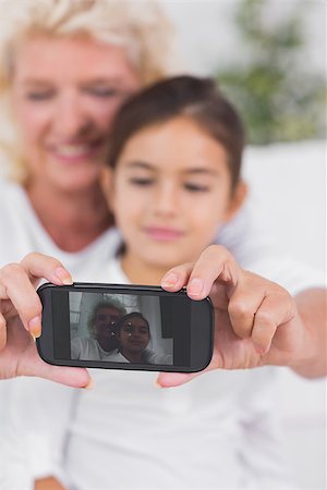 simsearch:400-06874610,k - Cheerful granddaughter and grandmother taking photos together on the sofa Foto de stock - Super Valor sin royalties y Suscripción, Código: 400-06874513