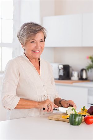 simsearch:400-06874653,k - Old woman cutting vegetables on a cutting board with a smile in kitchen Photographie de stock - Aubaine LD & Abonnement, Code: 400-06874658