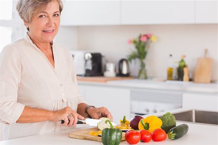 simsearch:400-06891385,k - Elderly woman cutting vegetables on a cutting board with a smile in kitchen Stock Photo - Budget Royalty-Free & Subscription, Code: 400-06874659