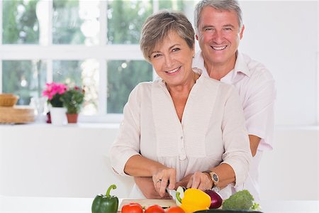 simsearch:400-06874610,k - Smiling woman cutting vegetables with her ??husband hugging her from behind in kitchen Foto de stock - Super Valor sin royalties y Suscripción, Código: 400-06874650