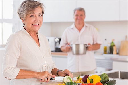simsearch:400-06874653,k - Old couple smiling preparing food in kitchen Photographie de stock - Aubaine LD & Abonnement, Code: 400-06874661