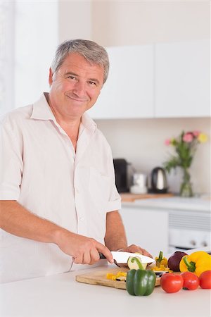simsearch:400-06874653,k - Old man smiling and chopping vegetables in kitchen Photographie de stock - Aubaine LD & Abonnement, Code: 400-06874663
