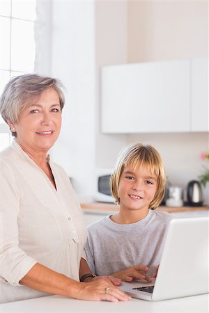 simsearch:400-06874653,k - Child and grandmother looking camera with a laptop in kitchen Photographie de stock - Aubaine LD & Abonnement, Code: 400-06874677