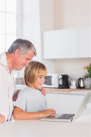 simsearch:400-06874653,k - Child and grandfather looking at laptop with smile in kitchen Photographie de stock - Aubaine LD & Abonnement, Code: 400-06874685