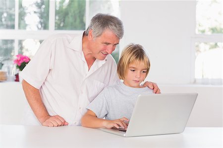 simsearch:400-06874653,k - Grandfather and child looking at laptop with smile in kitchen Photographie de stock - Aubaine LD & Abonnement, Code: 400-06874686