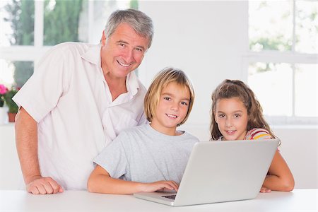 simsearch:400-06874653,k - Grandfather and children looking at the camera with laptop in front in kitchen Photographie de stock - Aubaine LD & Abonnement, Code: 400-06874689