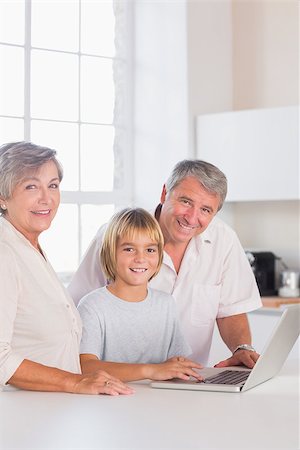 simsearch:400-06874653,k - Grandparents and child looking at camera with a laptop in kitchen Photographie de stock - Aubaine LD & Abonnement, Code: 400-06874682