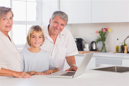 simsearch:400-06874653,k - Child and grandparents looking at the camera with a laptop in front in kitchen Photographie de stock - Aubaine LD & Abonnement, Code: 400-06874683