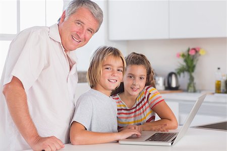 simsearch:400-06874653,k - Grandfather and children looking at the camera together with laptop in front in kitchen Photographie de stock - Aubaine LD & Abonnement, Code: 400-06874690