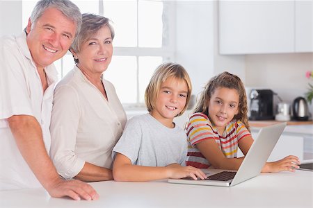 simsearch:400-06874653,k - Grandparents and children looking at the camera together with laptop in front in kitchen Photographie de stock - Aubaine LD & Abonnement, Code: 400-06874691
