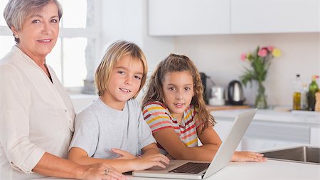 simsearch:400-06874653,k - Children and grandmother looking at the camera together with laptop in front in kitchen Photographie de stock - Aubaine LD & Abonnement, Code: 400-06874693