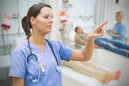 simsearch:400-06875952,k - Nurse in blue scrubs standing in hospital ward pointing to something Stockbilder - Microstock & Abonnement, Bildnummer: 400-06875765