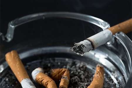 simsearch:400-06876304,k - Burning cigarette butt in ashtray on black background Stockbilder - Microstock & Abonnement, Bildnummer: 400-06876299
