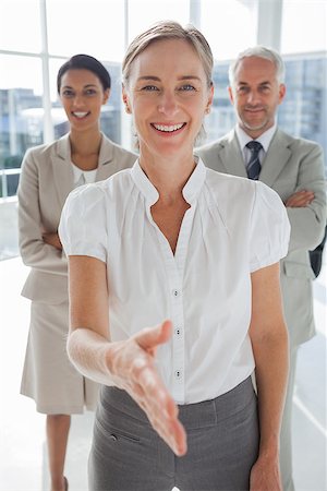 simsearch:400-06879270,k - Smiling businesswoman giving a handshake with colleagues behind standing together Stock Photo - Budget Royalty-Free & Subscription, Code: 400-06879294
