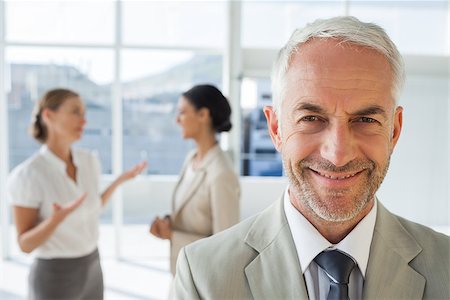 simsearch:400-06879270,k - Smiling businessman standing in front of colleagues talking together in their office Stock Photo - Budget Royalty-Free & Subscription, Code: 400-06879298