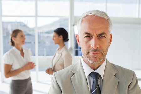 simsearch:400-06879270,k - Serious businessman standing while colleague are discussing together during working hours Stock Photo - Budget Royalty-Free & Subscription, Code: 400-06879299