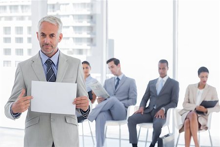 Serious businessman holding a blank notice with people waiting behind Stock Photo - Budget Royalty-Free & Subscription, Code: 400-06879406