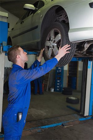 simsearch:400-06870097,k - Side view of male mechanic examining car tire in workshop Foto de stock - Super Valor sin royalties y Suscripción, Código: 400-06870050