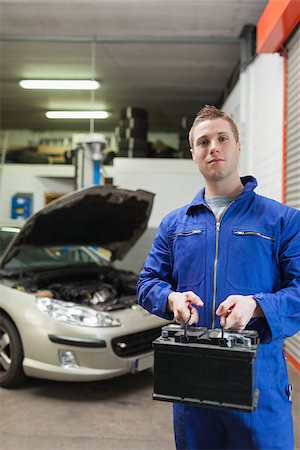 simsearch:400-06870131,k - Portrait of confident auto mechanic with car battery in workshop Photographie de stock - Aubaine LD & Abonnement, Code: 400-06870132