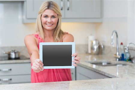 Portrait of casual young woman holding out digital tablet in the kitchen at home Photographie de stock - Aubaine LD & Abonnement, Code: 400-06871128