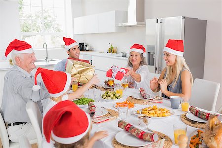 simsearch:400-06871557,k - Family wearing santa hats swapping christmas presents at dinner table Photographie de stock - Aubaine LD & Abonnement, Code: 400-06871634
