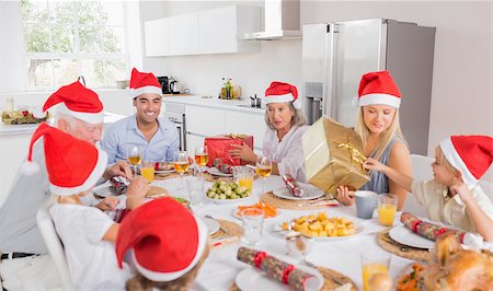 Smiling family at the dinner table at christmas exchanging gifts wearing santa hats Stock Photo - Budget Royalty-Free & Subscription, Code: 400-06871636