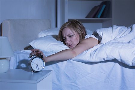 Irritated young woman in bed extending hand to alarm clock at home Stock Photo - Budget Royalty-Free & Subscription, Code: 400-06872230