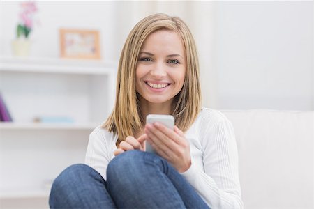 simsearch:400-06872352,k - Portrait of young woman with mobile phone sitting on couch at home Foto de stock - Royalty-Free Super Valor e Assinatura, Número: 400-06872372