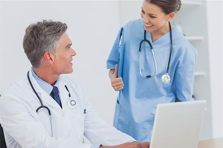 simsearch:6109-06781530,k - Doctor with a clipboard talking to a colleague while he is using a laptop Photographie de stock - Aubaine LD & Abonnement, Code: 400-06884206