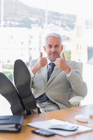 Happy businessman giving thumbs up with feet up on his desk Photographie de stock - Aubaine LD & Abonnement, Code: 400-06884339