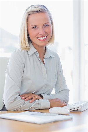 simsearch:400-06883455,k - Young businesswoman smiling at camera at her desk Photographie de stock - Aubaine LD & Abonnement, Code: 400-06884358